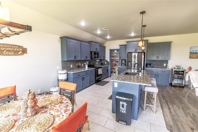 kitchen featuring a breakfast bar, sink, appliances with stainless steel finishes, an island with sink, and light stone countertops