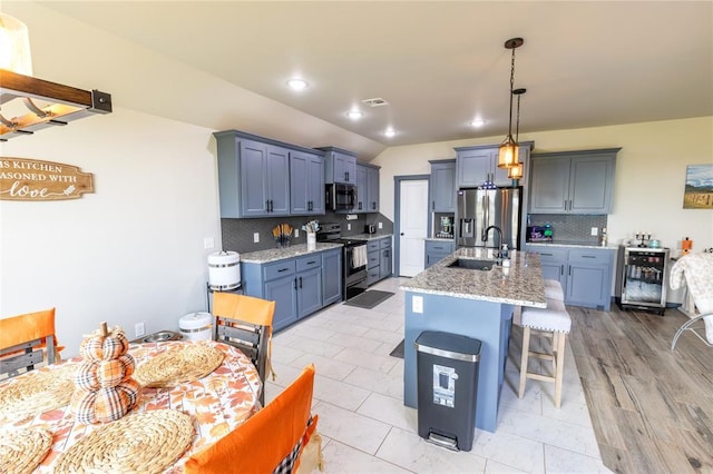 kitchen with sink, electric range oven, stainless steel refrigerator with ice dispenser, light stone countertops, and an island with sink