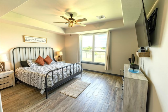 bedroom with a raised ceiling, wood-type flooring, and ceiling fan