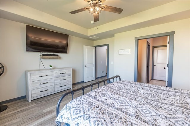 bedroom with light hardwood / wood-style flooring, a raised ceiling, and ceiling fan