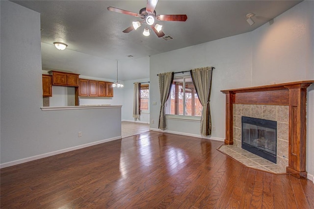 unfurnished living room with dark wood-type flooring, ceiling fan, and a tiled fireplace