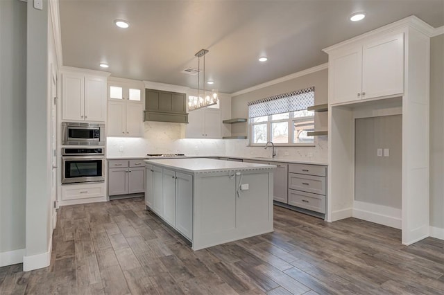 kitchen with appliances with stainless steel finishes, pendant lighting, tasteful backsplash, white cabinetry, and a center island