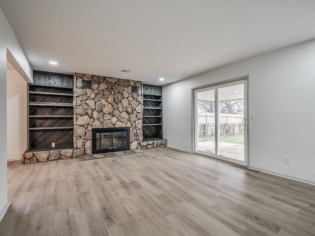 unfurnished living room with a stone fireplace, built in features, and light hardwood / wood-style floors