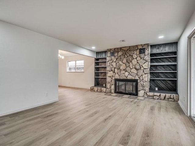 unfurnished living room featuring a stone fireplace, built in features, and light hardwood / wood-style flooring