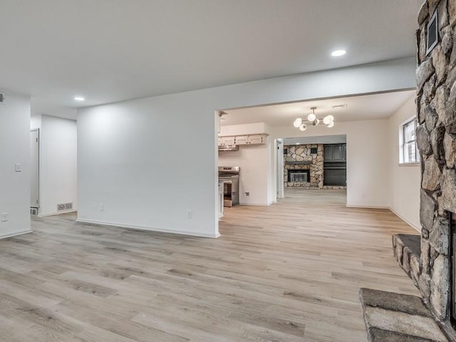 unfurnished living room with an inviting chandelier, a stone fireplace, and light hardwood / wood-style flooring