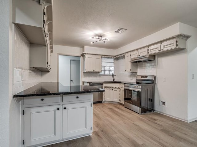 kitchen with white cabinetry, dark stone countertops, light hardwood / wood-style floors, kitchen peninsula, and stainless steel appliances