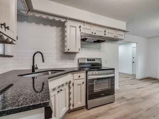 kitchen featuring sink, dark stone countertops, tasteful backsplash, stainless steel range, and light wood-type flooring