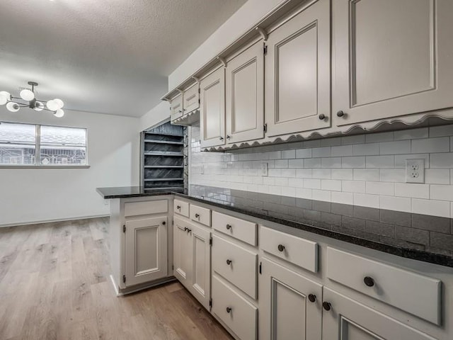 kitchen with light hardwood / wood-style flooring, backsplash, a notable chandelier, a textured ceiling, and kitchen peninsula