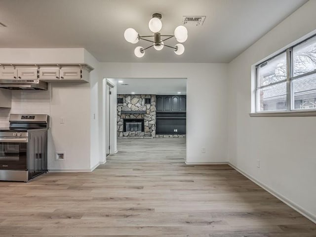 kitchen featuring tasteful backsplash, a chandelier, light hardwood / wood-style flooring, electric stove, and a fireplace