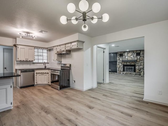 kitchen featuring sink, appliances with stainless steel finishes, a fireplace, light hardwood / wood-style floors, and decorative backsplash