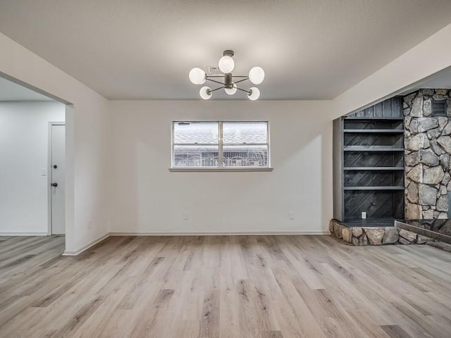 unfurnished dining area with an inviting chandelier, built in features, light wood-type flooring, and a fireplace