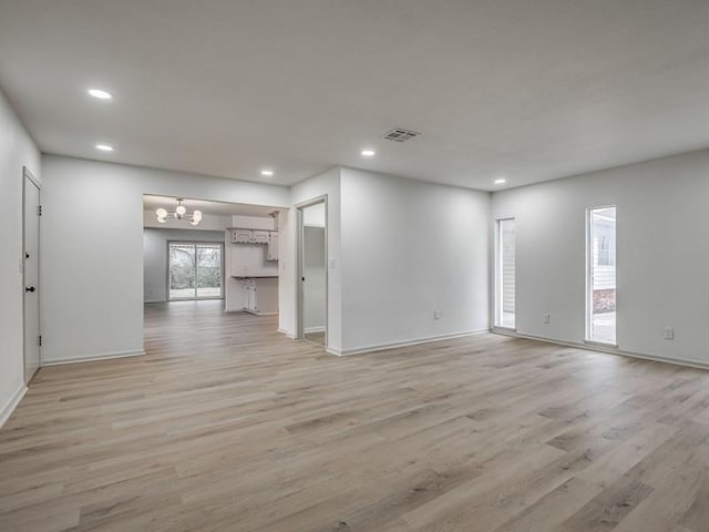 unfurnished living room with an inviting chandelier and light hardwood / wood-style floors