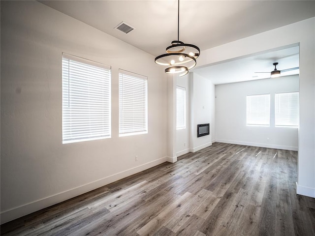 unfurnished living room featuring ceiling fan with notable chandelier, a healthy amount of sunlight, hardwood / wood-style floors, and heating unit