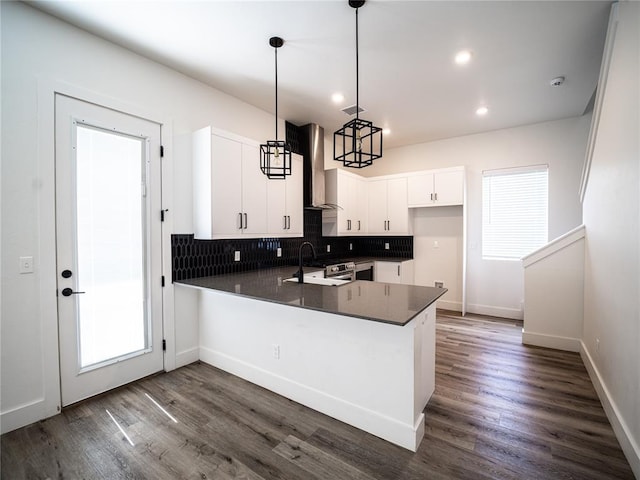 kitchen featuring sink, white cabinets, hanging light fixtures, kitchen peninsula, and wall chimney range hood