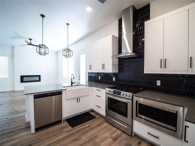 kitchen featuring pendant lighting, sink, white cabinetry, stainless steel appliances, and wall chimney exhaust hood