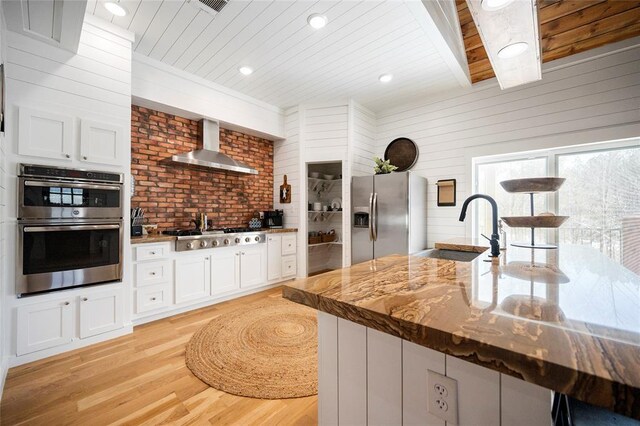kitchen with wall chimney exhaust hood, appliances with stainless steel finishes, a sink, wood ceiling, and light wood-style flooring