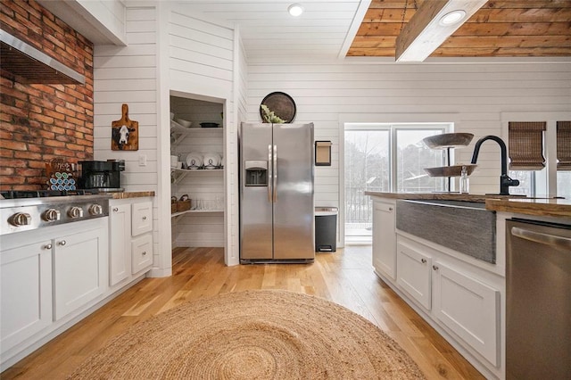 kitchen with stainless steel appliances, light wood-type flooring, a sink, wood ceiling, and wood walls