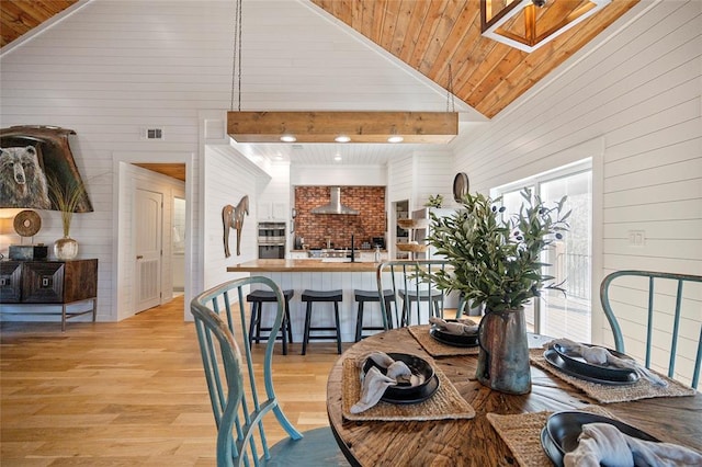 dining room featuring wooden walls, light wood-type flooring, lofted ceiling, a skylight, and wooden ceiling