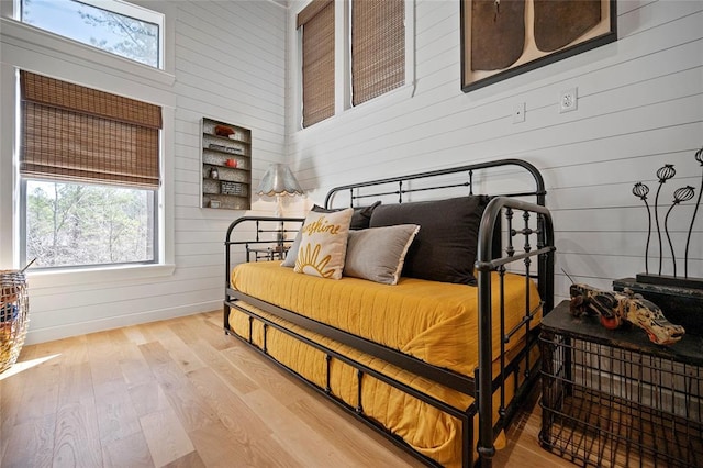 bedroom with wooden walls, multiple windows, and light wood-style floors