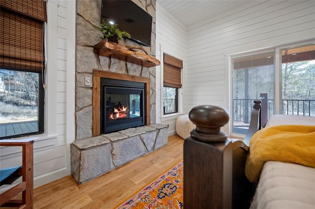 living area with wood finished floors, a stone fireplace, wooden walls, and healthy amount of natural light