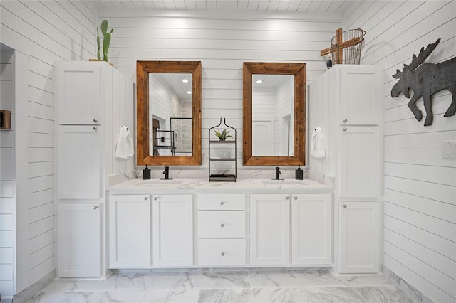 bathroom featuring wood walls, marble finish flooring, and double vanity