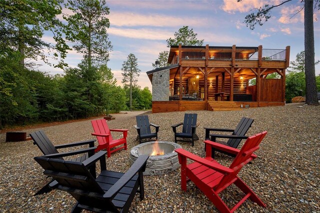 back of house at dusk with an outdoor fire pit and stone siding