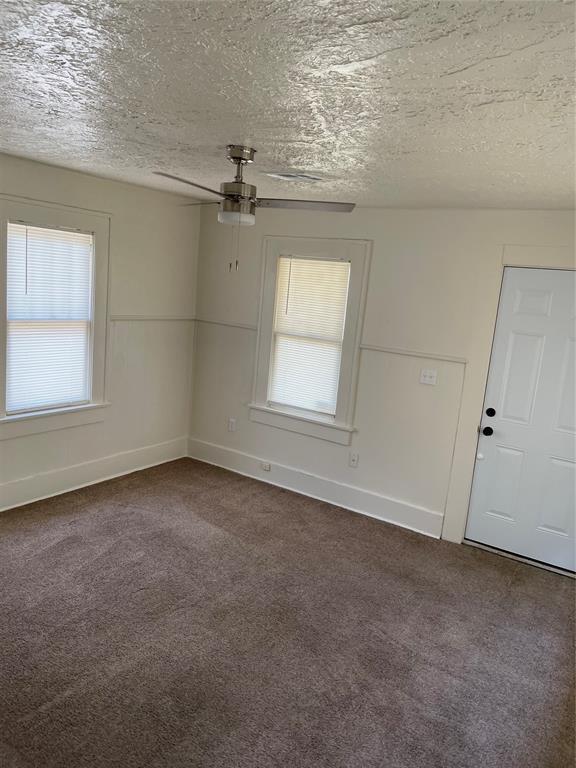 carpeted empty room with ceiling fan, a textured ceiling, and a wealth of natural light