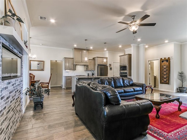 living room featuring ornate columns, wood-type flooring, sink, ceiling fan, and crown molding