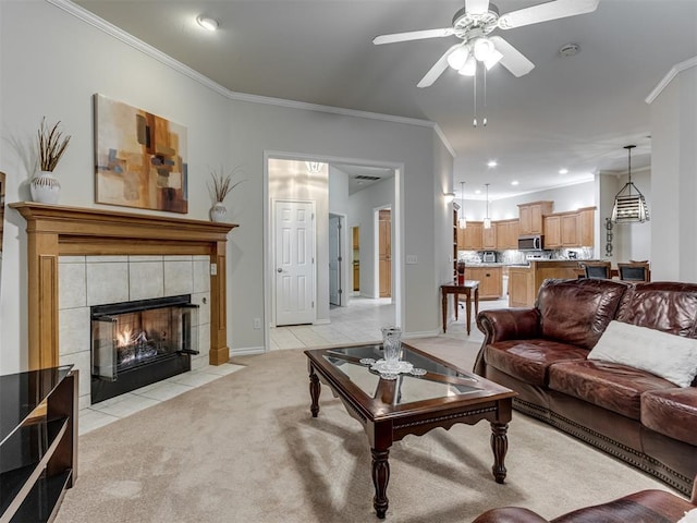 living room with a tile fireplace, ornamental molding, light carpet, and ceiling fan