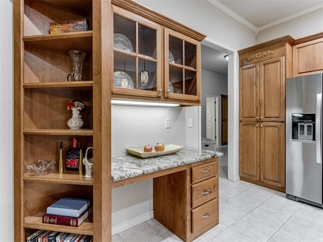 kitchen featuring light tile patterned floors, stainless steel fridge, built in desk, ornamental molding, and light stone countertops