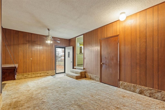 spare room with ceiling fan, carpet flooring, a textured ceiling, and wood walls