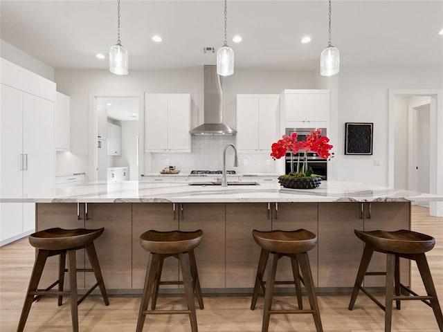 kitchen featuring modern cabinets, light wood-type flooring, wall chimney range hood, white cabinetry, and backsplash