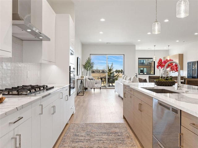 kitchen with appliances with stainless steel finishes, open floor plan, a sink, wall chimney range hood, and backsplash