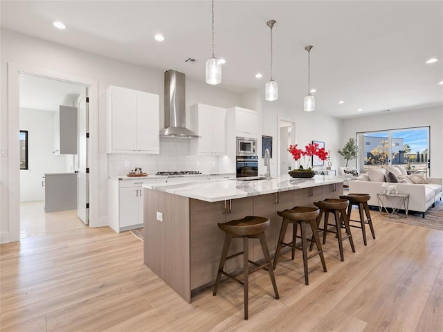 kitchen featuring wall chimney exhaust hood, decorative backsplash, light wood-style flooring, and stainless steel appliances