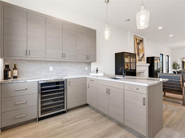 kitchen featuring gray cabinets, decorative backsplash, light wood-style floors, beverage cooler, and a peninsula