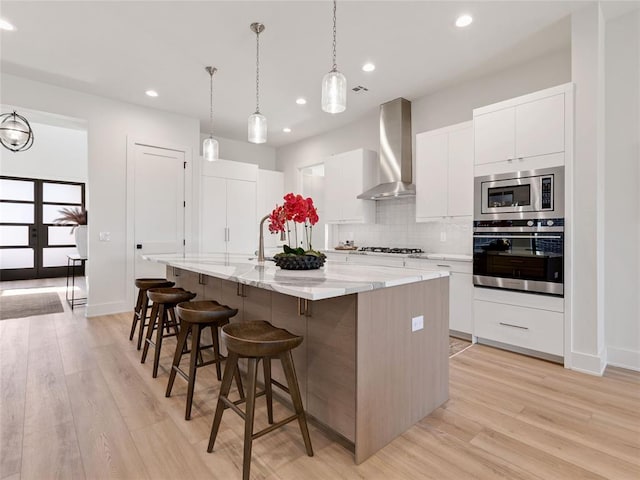 810 NW 72nd St, Oklahoma City, OK 73116 - kitchen featuring stainless steel appliances, tasteful backsplash, an island with sink, light wood-type flooring, and wall chimney range hood