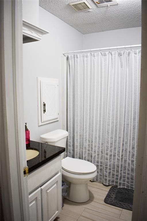 bathroom featuring a shower with shower curtain, vanity, wood-type flooring, a textured ceiling, and toilet