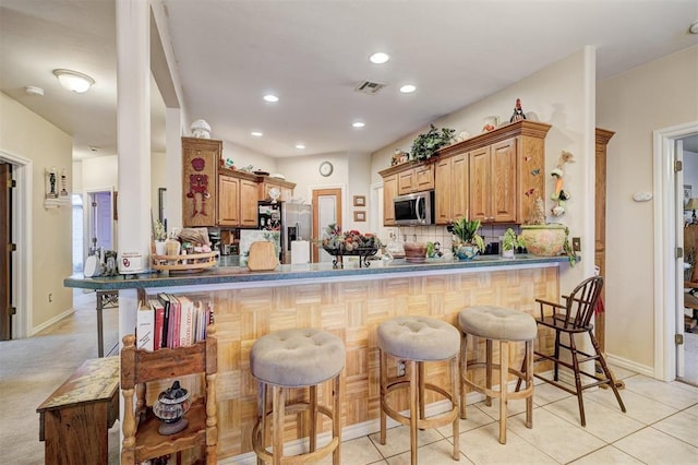 kitchen featuring tasteful backsplash, appliances with stainless steel finishes, a kitchen bar, and kitchen peninsula