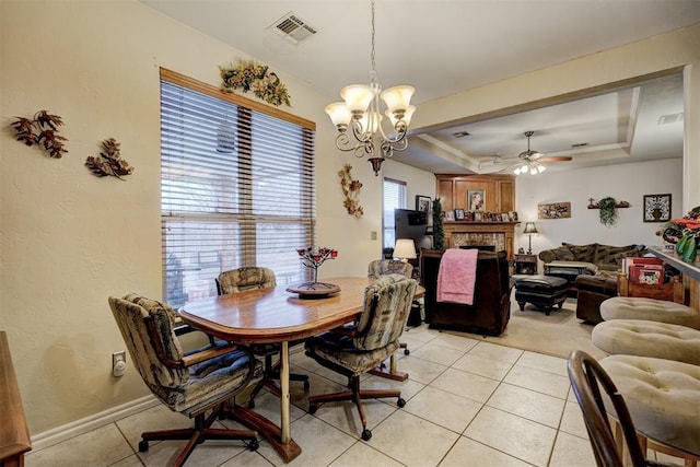 dining space featuring a tray ceiling, ceiling fan with notable chandelier, a brick fireplace, and light tile patterned floors