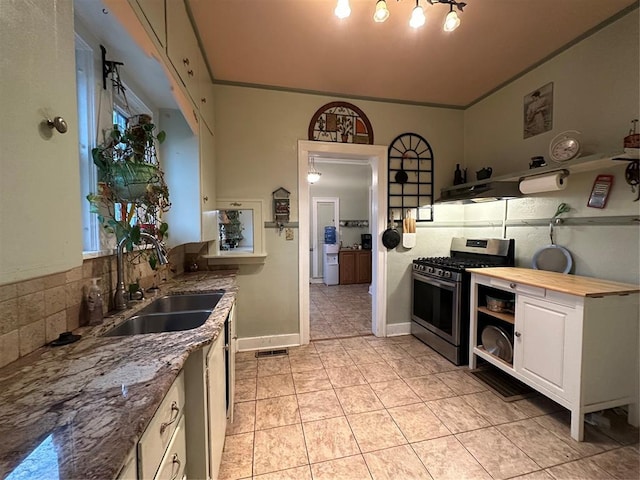 kitchen with stainless steel gas range, sink, white cabinetry, light tile patterned floors, and decorative backsplash