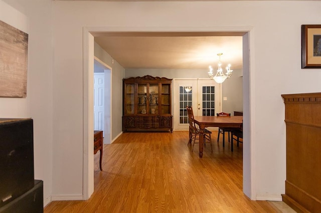 dining space with a chandelier, light wood-type flooring, and french doors