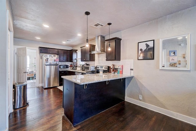 kitchen with dark brown cabinetry, a peninsula, appliances with stainless steel finishes, wall chimney exhaust hood, and dark wood-style flooring