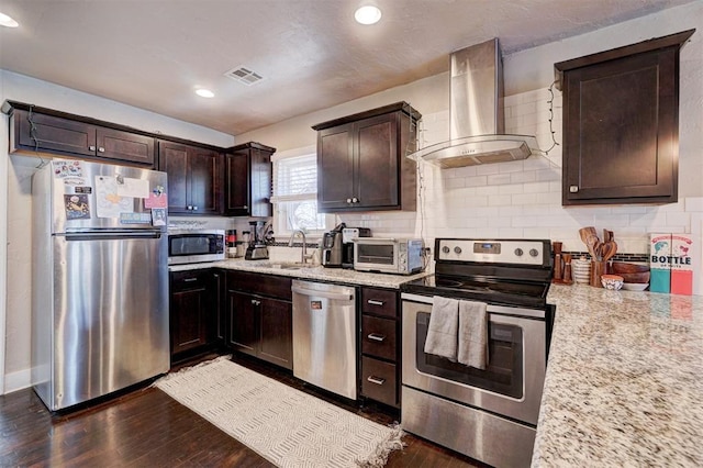 kitchen featuring a sink, dark wood-type flooring, dark brown cabinets, appliances with stainless steel finishes, and wall chimney range hood