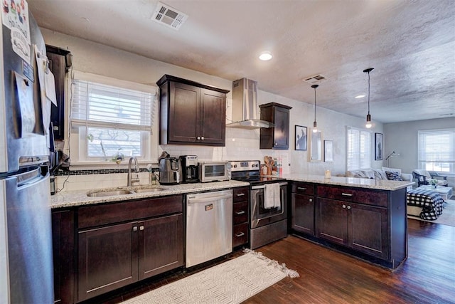 kitchen with visible vents, wall chimney range hood, appliances with stainless steel finishes, a peninsula, and a sink