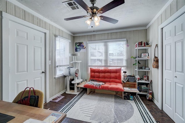 living area featuring crown molding, a ceiling fan, visible vents, and a wealth of natural light