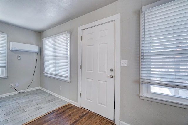 foyer entrance featuring wood finished floors, a healthy amount of sunlight, baseboards, and a wall mounted AC