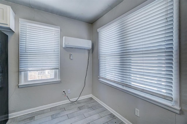 spare room with an AC wall unit, wood finished floors, and baseboards