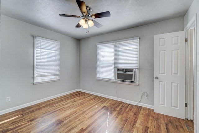 spare room featuring cooling unit, wood finished floors, baseboards, ceiling fan, and a textured ceiling