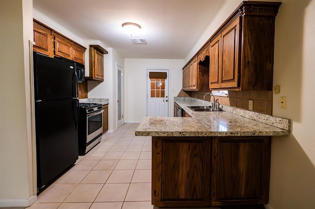 kitchen featuring light tile patterned flooring, black refrigerator, sink, kitchen peninsula, and stainless steel range with gas stovetop