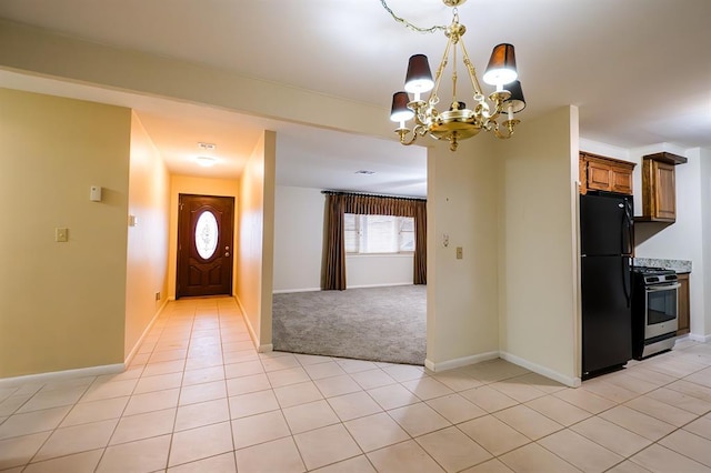 kitchen featuring light tile patterned flooring, a chandelier, hanging light fixtures, stainless steel gas range oven, and black fridge